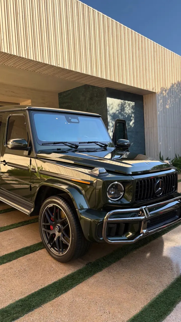 A dark green Mercedes G-Wagon, freshly waxed, in front of a modern house