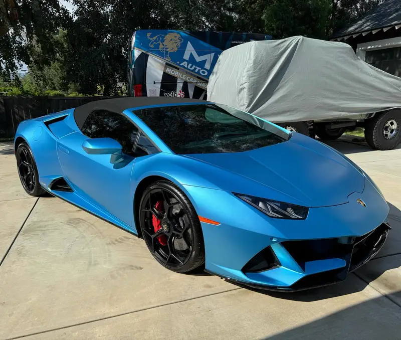 A light blue Lamborghini Huracán in a driveway, the MVP van behind it