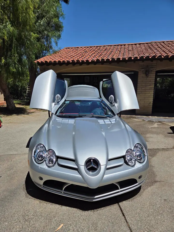 A silver Mercedes SLR McLaren with its doors up, in a driveway